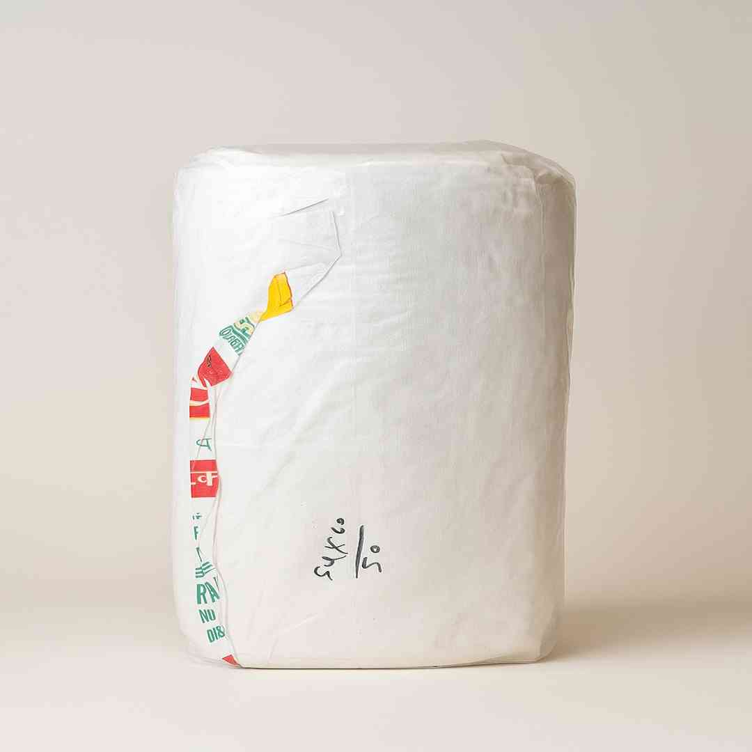 large cylindrical roll wrapped in white printed fabric packaging, placed upright on beige surface